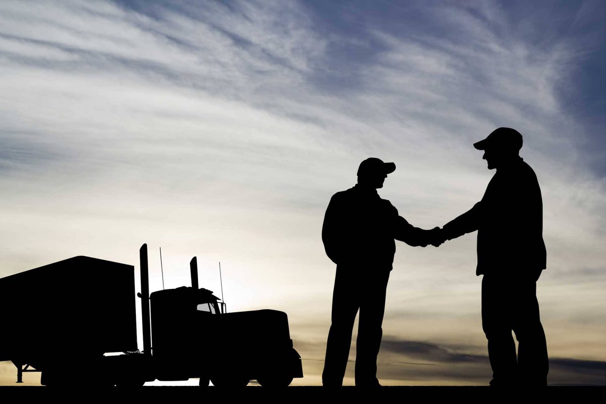 silhouette of two men shaking hands near a semi truck